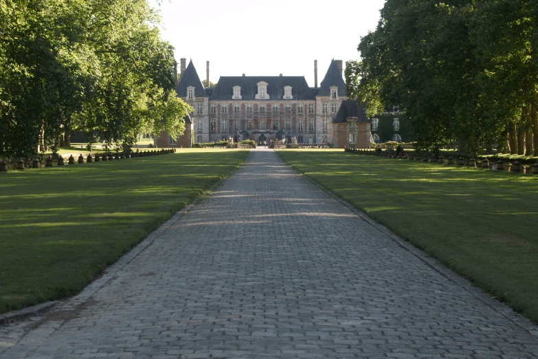 a path leading to an elegant house with trees lining the sides