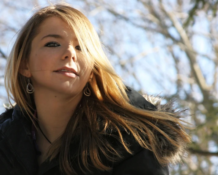 a woman with long hair wearing earrings and coat