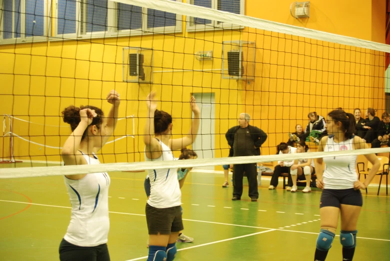 four women are playing volleyball and one is trying to block the ball