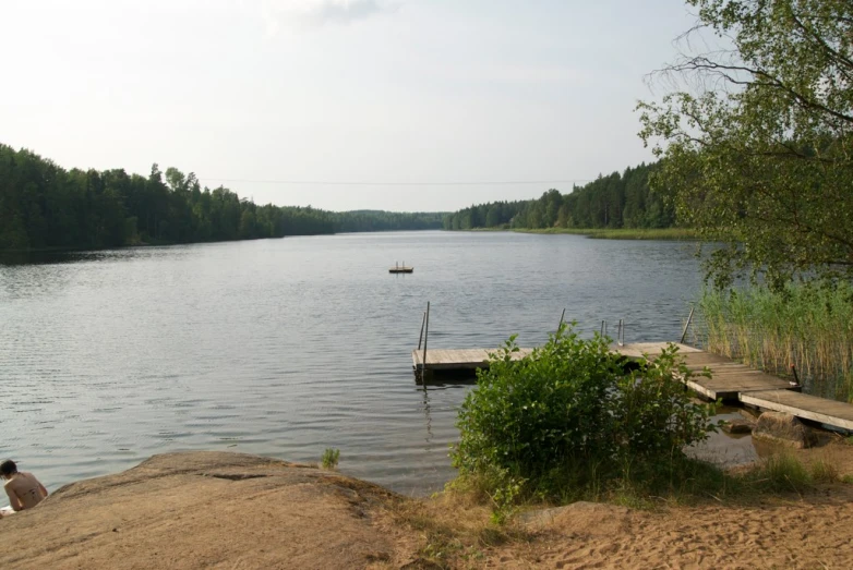 a person sitting on a beach near a lake and a boat in the water