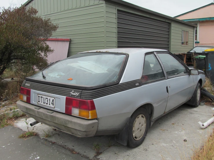 an abandoned car in front of a house and a garbage can