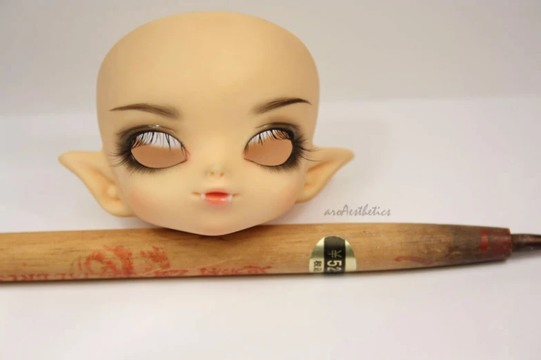 doll head next to brown wooden handle on white surface