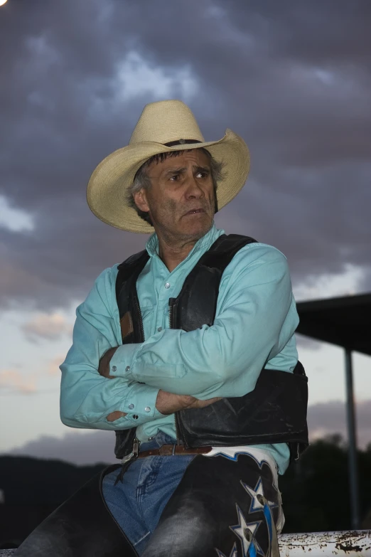 the man is wearing a cowboy hat and sitting against a rail