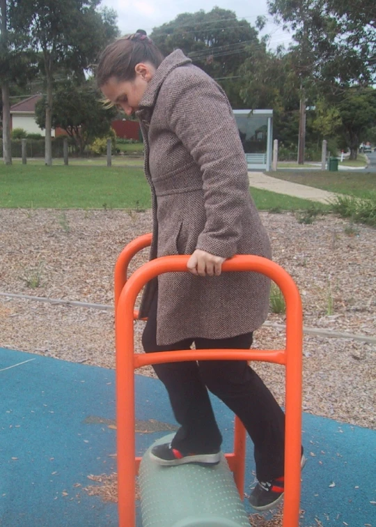a woman playing on a red and orange metal park structure