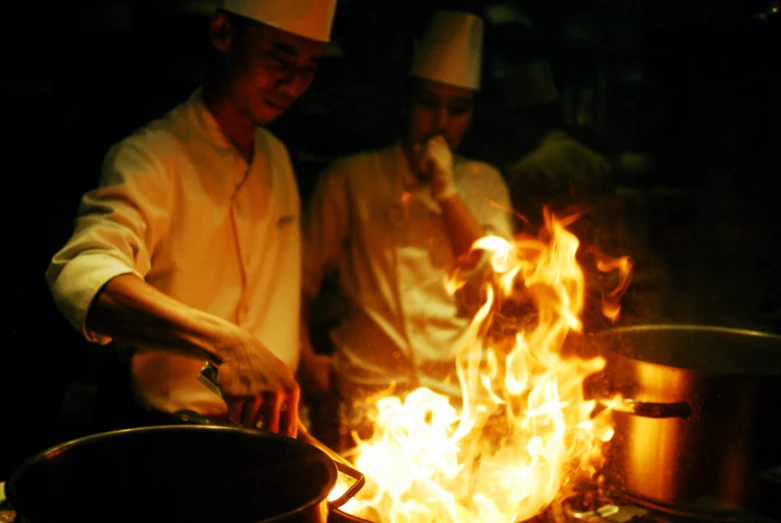 two chefs are cooking food in the flames