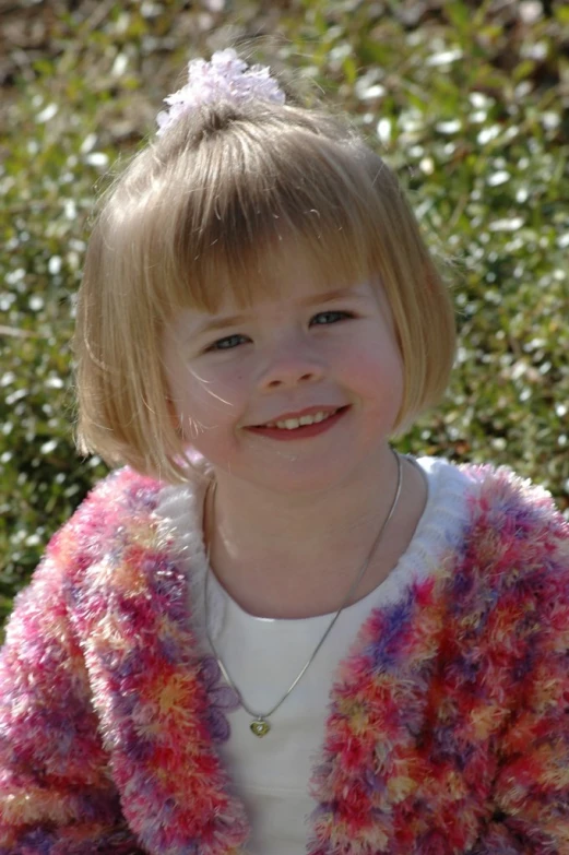 a  smiles at the camera as she wears a multi - colored knitted sweater