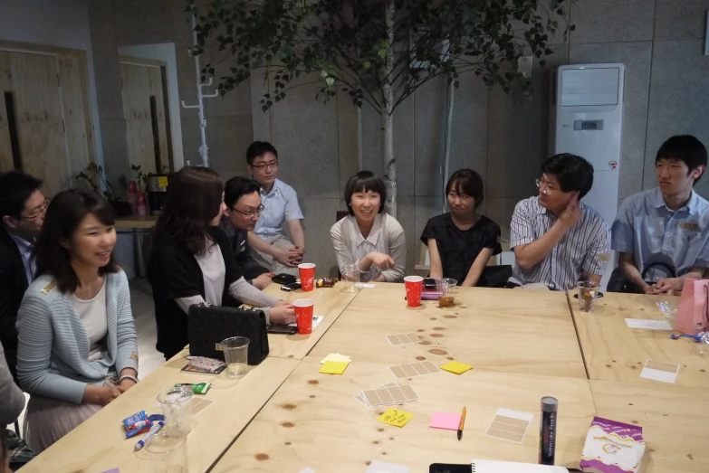 people are seated at a wooden table having conversation