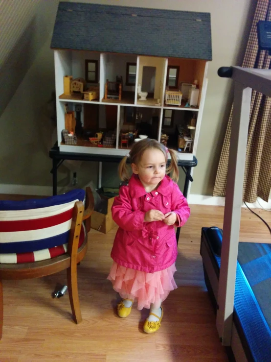 a little girl standing in a living room by a dollhouse
