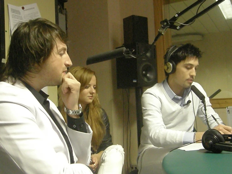 man in suit sitting in front of microphone while another person holds his headphones up in front of him