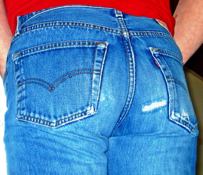 the back of a women wearing blue jeans with torn knee holes