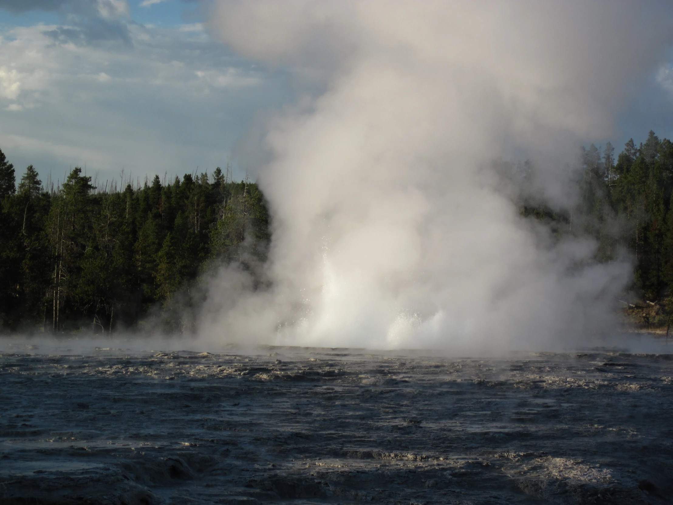 steam coming from a geyser is seen on the side of a river