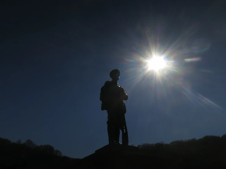 a man is standing on the edge of a rock in front of the sun