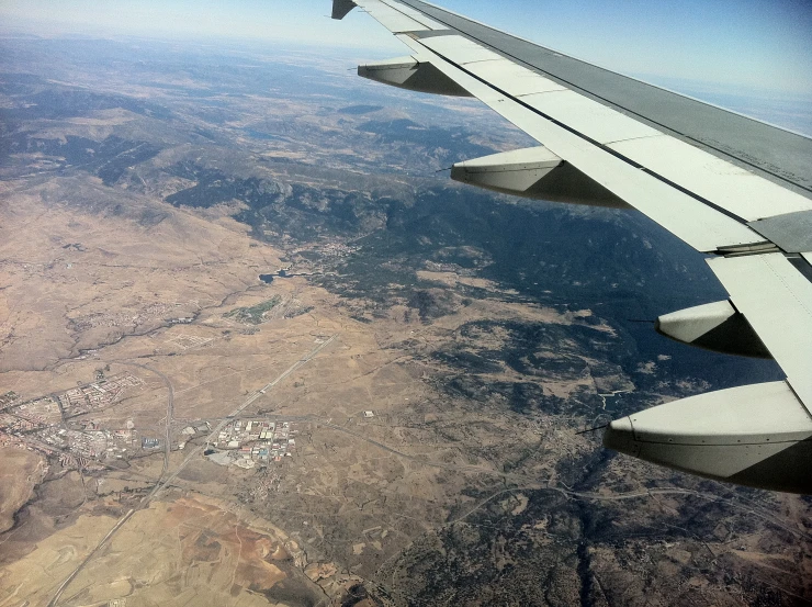 an airplane wing over a desert and a city