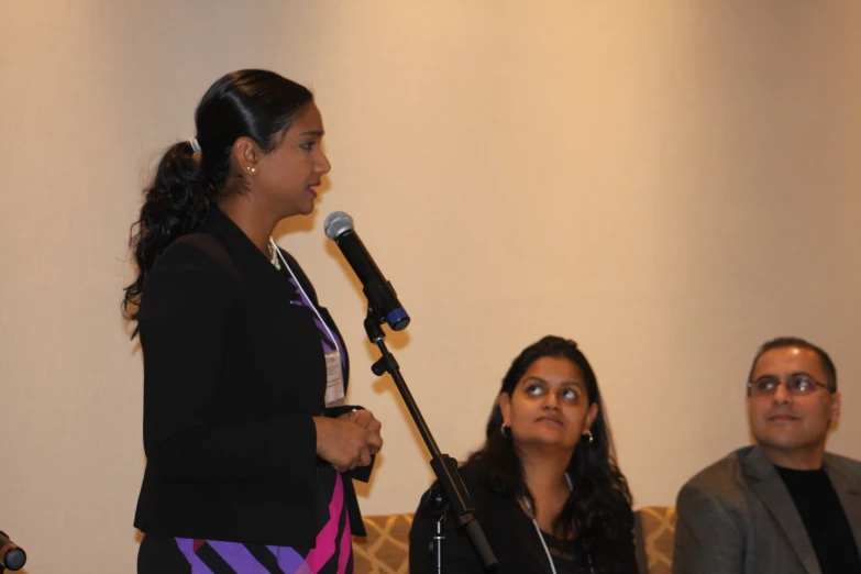 a woman speaking into a microphone while people sit