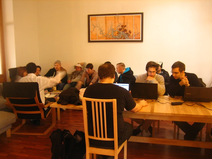a bunch of people sitting around a wooden table working on their laptops