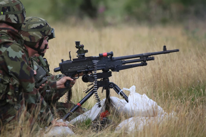 two soldiers are in the tall grass with their machine gun