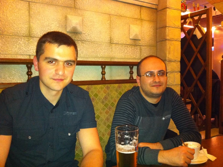 two men sitting down at a table with drinks