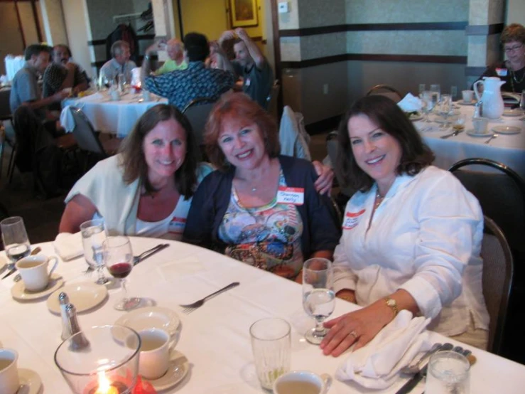 three women sit at a table in the center of a restaurant, both smiling