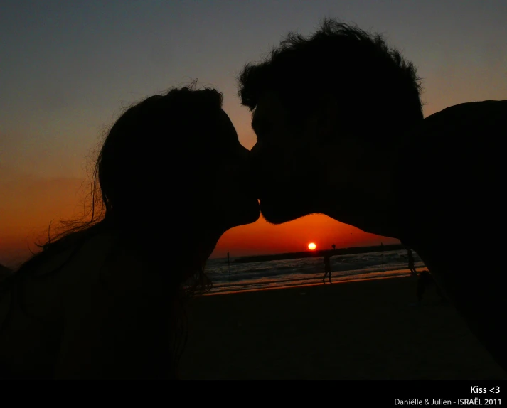 a man kissing a woman at the beach with the sun setting in the background