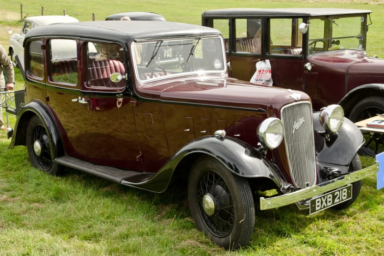 an old, maroon - hued, antique car sits on grass