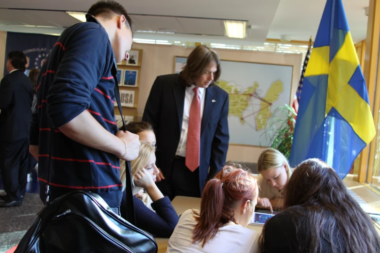 people standing around a wooden table in front of flags