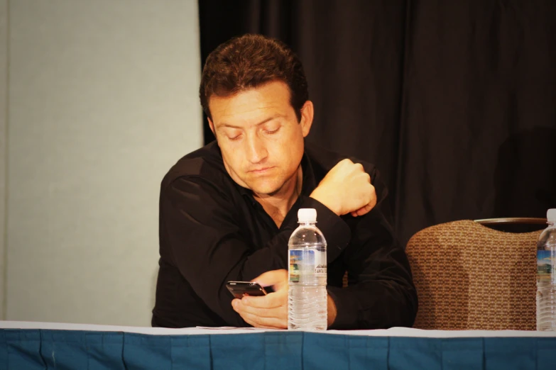 a man sitting at a table looking down at his cell phone