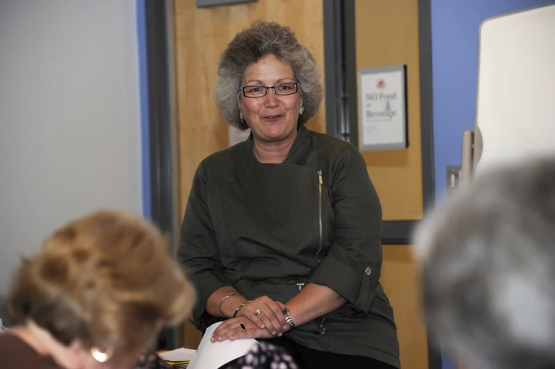 an older woman with glasses sits in a chair near some other women