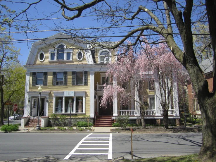 a yellow house with a white porch has a tree in front