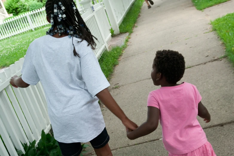 a  is holding the hand of a younger girl in front of a white fence