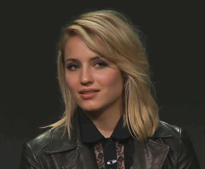 the blond woman has her eyes shut as she is sitting in front of a dark background
