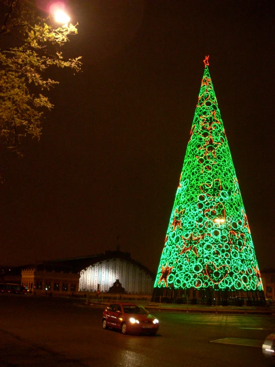 a lighted christmas tree and car in a city street at night