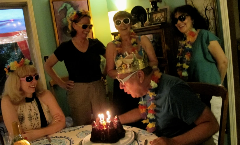 a man wearing leis lights a candle on a cake while surrounded by other people