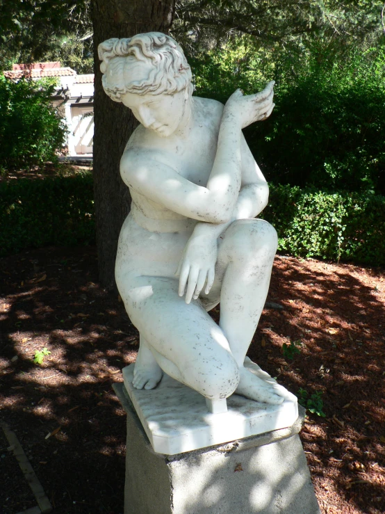 a white statue of a seated human holding onto a tree