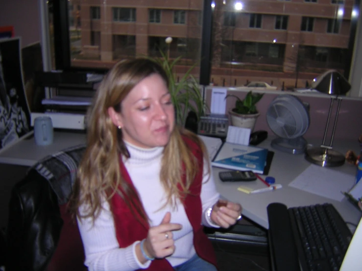 a woman sitting at a computer desk with a cell phone