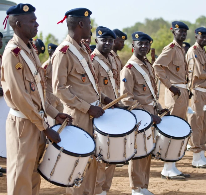 several men in dress uniforms hold drums and look around