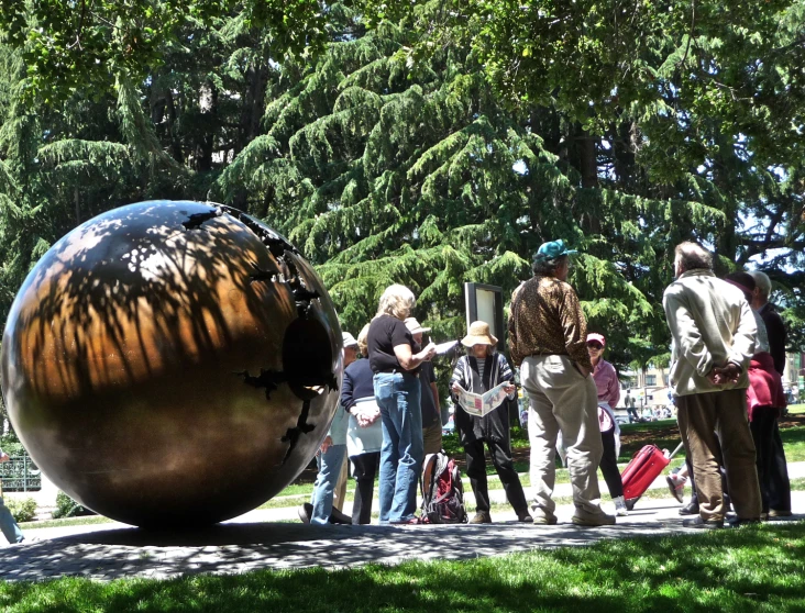 people are walking around an art object in the middle of a park