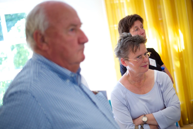 people stand and talk in a room with yellow curtains