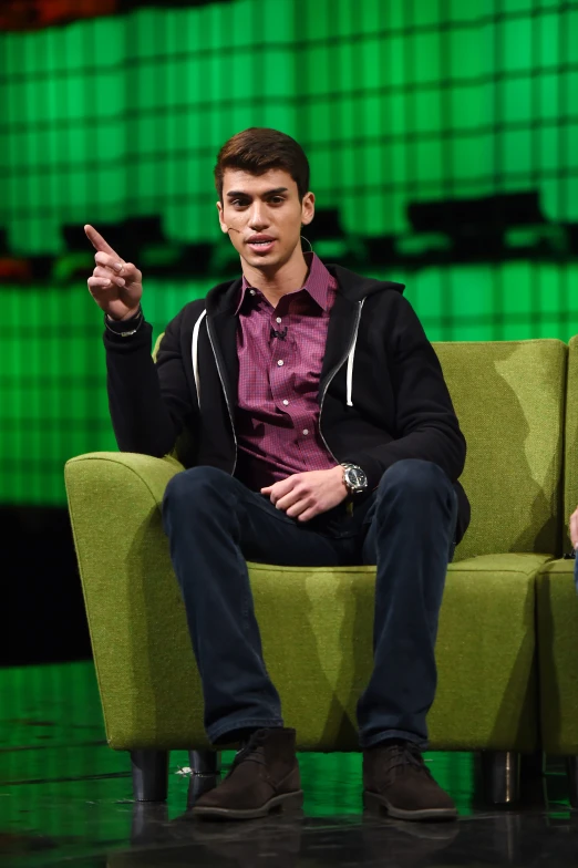 a young man in black jacket sitting on green chair