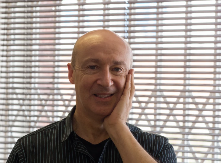 an older man with a bald head smiles while standing in front of a window