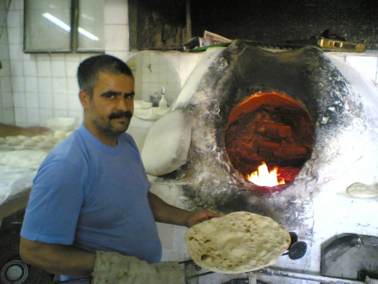 a man in blue shirt cooking a fire and making pizzas