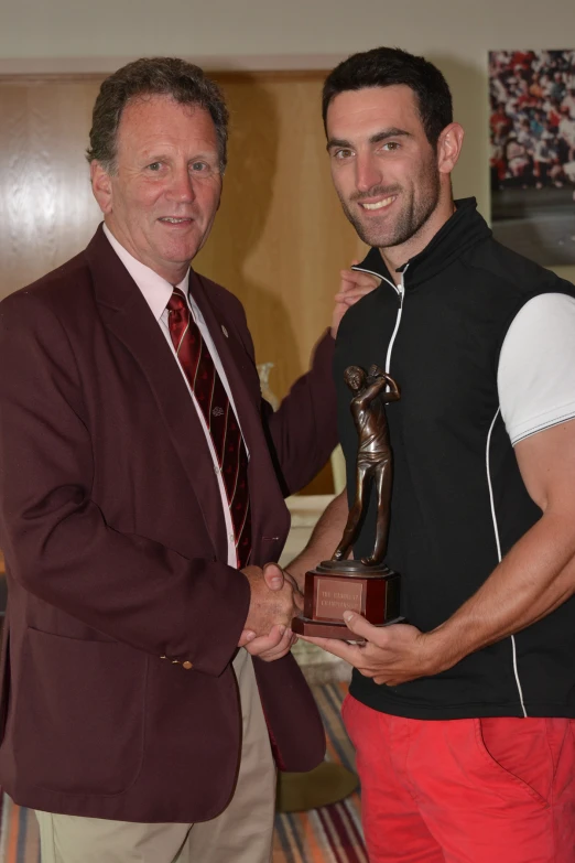 two men in suits posing for a picture, one holding a trophy