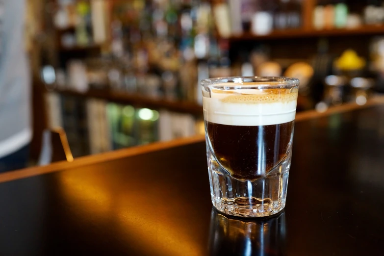 a glass on a bar, with a beverage in the background