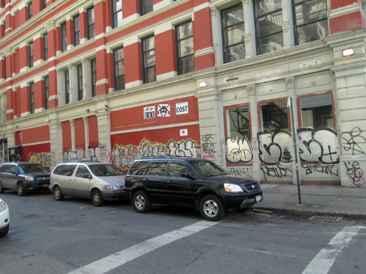 several cars parked on a street in front of a large building with graffiti on it