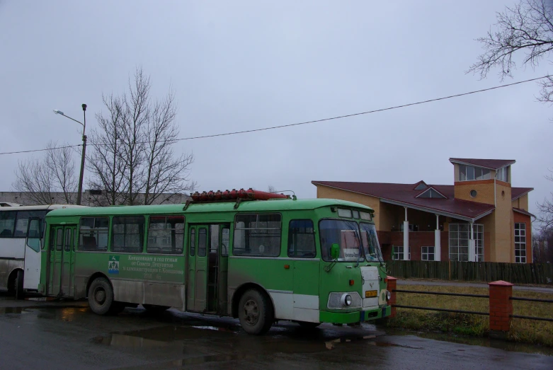 a green and white bus parked next to a wooden fence