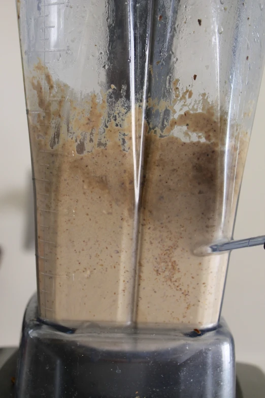 a silver blender with brown liquid and some spoons