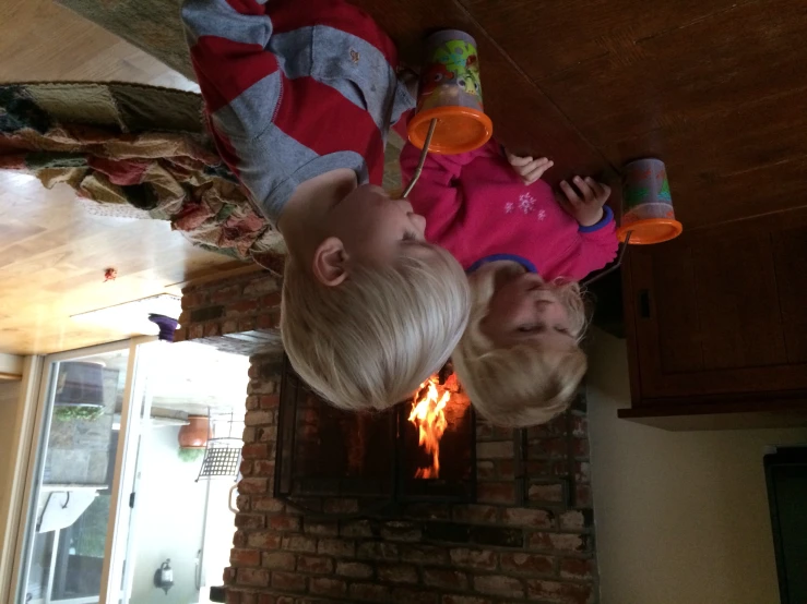 two small s are drinking beverages near a fire place