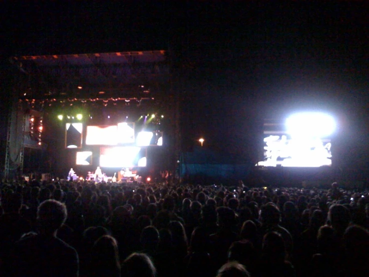 a view from the back of an outdoor concert, of several people in the audience with lights on their shoulders