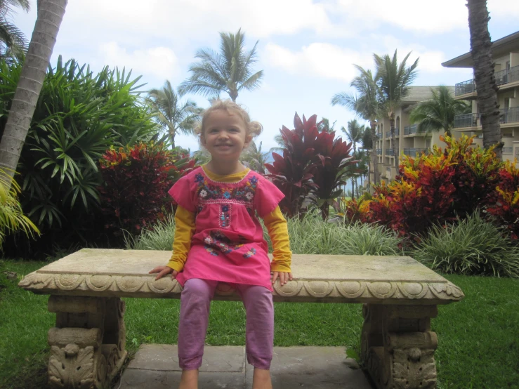 a little girl sitting on a bench at the beach