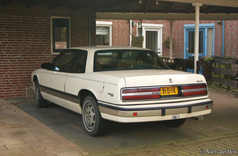 an old, white car is parked near a brick building