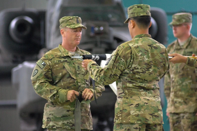 two army men in camo clothes standing near a helicopter